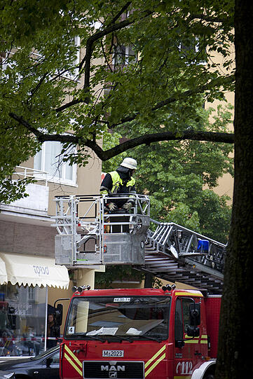 Ein Feuerwehrmabb fährt mit dem Kran nach oben. Seine Kollegen...