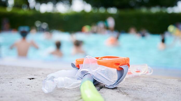 Eine Taucherbrille und Schnorchel liegen in einem Schwimmbad am Beckenrand.
