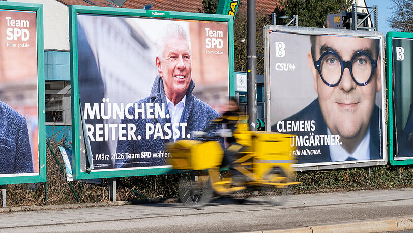 Eine Postbotin fährt an großflächige Plakate der Bürgermeisterkandidaten für SPD und CSU vorbei, die an einer Strasse im Norden der bayerischen Landeshauptstadt nebeneinander hängen. Die nächsten Kommunalwahl finden am 8. März 2026 statt.