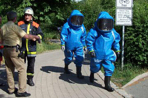 Geschützt durch Spezial-Anzüge (rechts) durchkämmen Feuerwehrleute das gesamte Gelände, um mögliche Opfer zu finden.