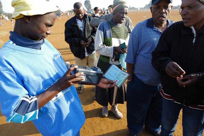 Ein Wahlbeauftragter in Südafrika scannt den Ausweis eines Wählers.