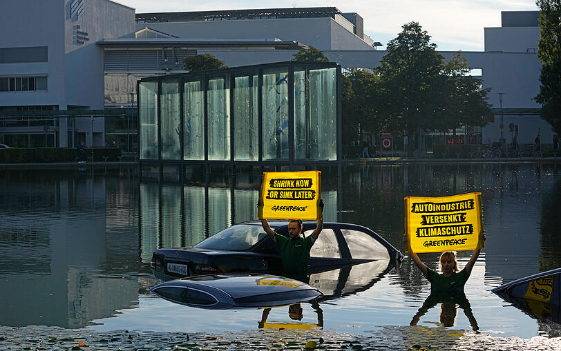 Umweltaktivisten von Greenpeace demonstrieren am Pressetag bei der Auto- und Verkehrsmesse IAA in der Messe München im See vor dem Haupteingang.