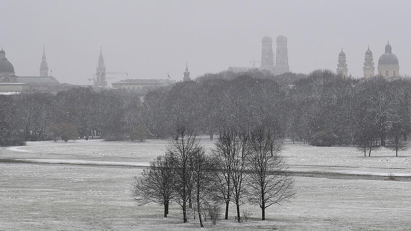 Die Staatskanzlei (l), die Frauenkirche (M) und die Theatienerkirche (r) sind vom Monopteros aus mit dem Englischen Garten bei Schnee zu sehen.