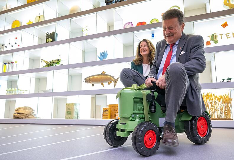 Wolfang Heckl, Generaldirektor des Deutschen Museum, sitzt während der Eröffnung der ersten neuen Dauerausstellung „Landwirtschaft und Ernährung“, die im Deutschen Museum präsentiert wird, auf einem Spielzeug-Traktor. Hinter ihm lacht Maria Thon, Geschäftsführerin der BayWa Stiftung. Das Museum wird seit geraumer Zeit saniert.
