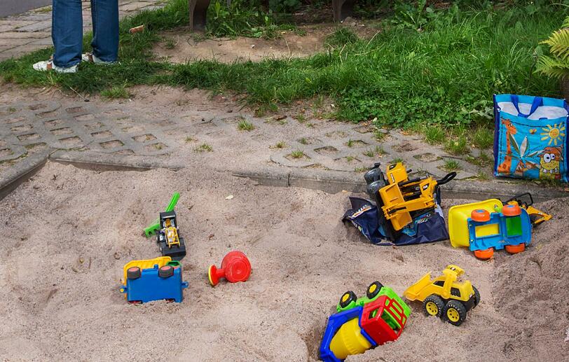 Spielzeug liegt in einem Sandkasten vor dem Gebäude.