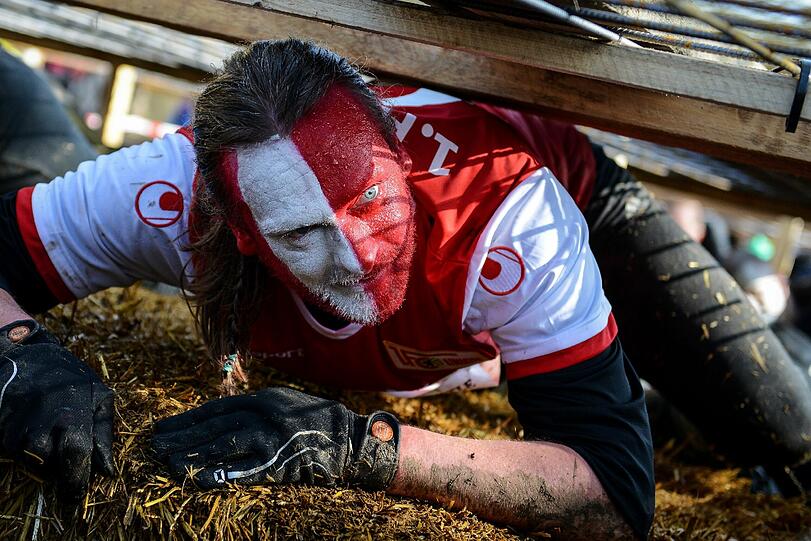 Mit bemalten Gesicht kämpft sich dieser Teilnehmer am Kriech-Hindernis vorbei.