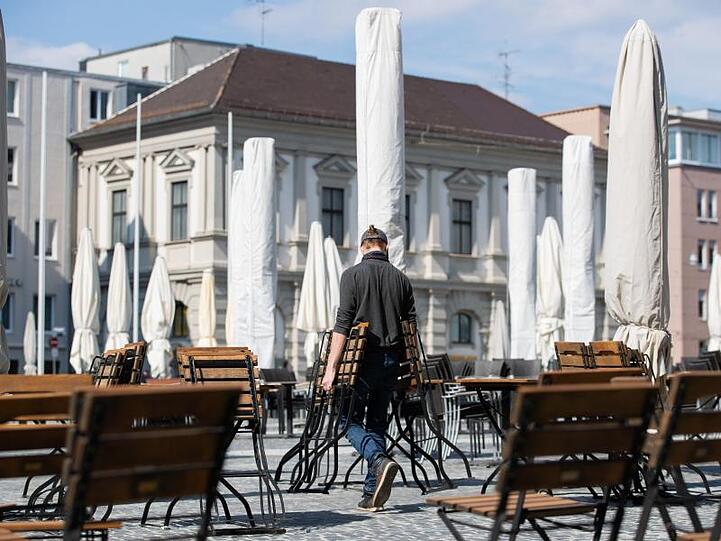 Ein Mann trägt Stühle auf den Rathausplatz in Augsburg. Foto: Tom Weller/dpa/Archivbild