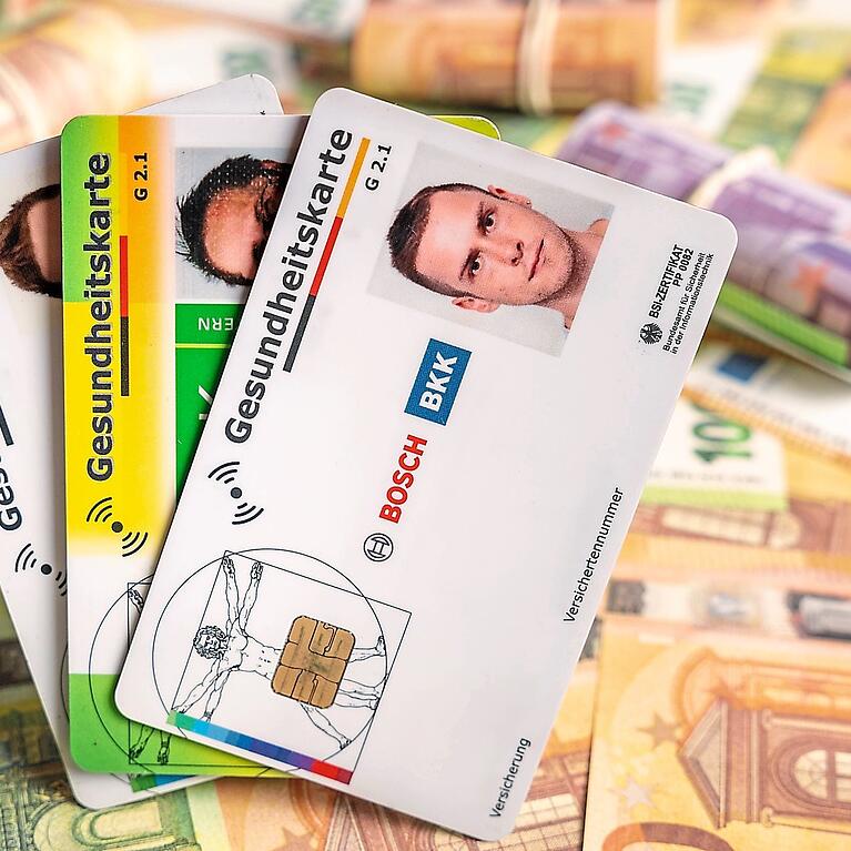 Hinter verschiedenen Gesundheitskarten liegen Geldscheine und B&uuml;ndel.