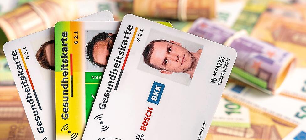 Hinter verschiedenen Gesundheitskarten liegen Geldscheine und B&uuml;ndel.