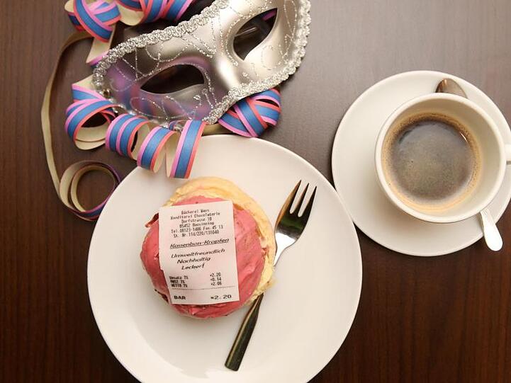 Ein Krapfen mit einem Kassenbon aus Fondant, einer essbaren Zuckermasse und eine Tasse Kaffee. Foto: Tobias Hase/dpa