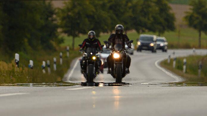 Zwei Biker fahren über eine Landstraße.