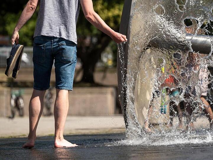 Ein Mann kühlt sich an einem Brunnen ab.