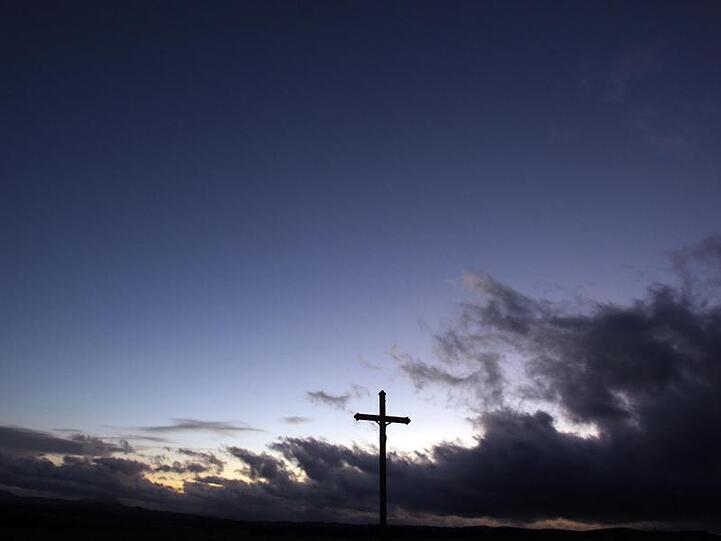 Wolken ziehen hinter einem Wegkreuz über das Voralpenland. Foto: picture alliance / dpa