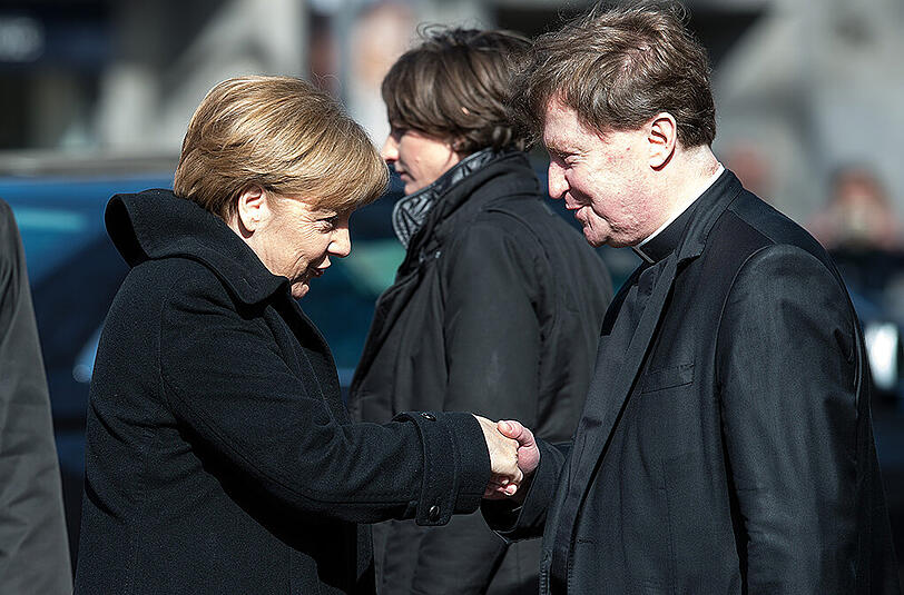 Bundeskanzlerin Angela Merkel wird von einem Geistlichen begrüßt.
