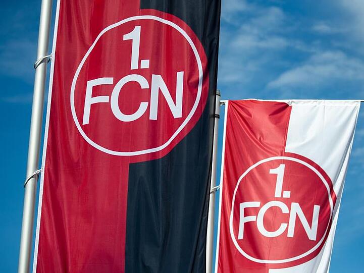 Das Logo des 1. FC Nürnberg steht auf Fahnen. Foto: Daniel Karmann/dpa