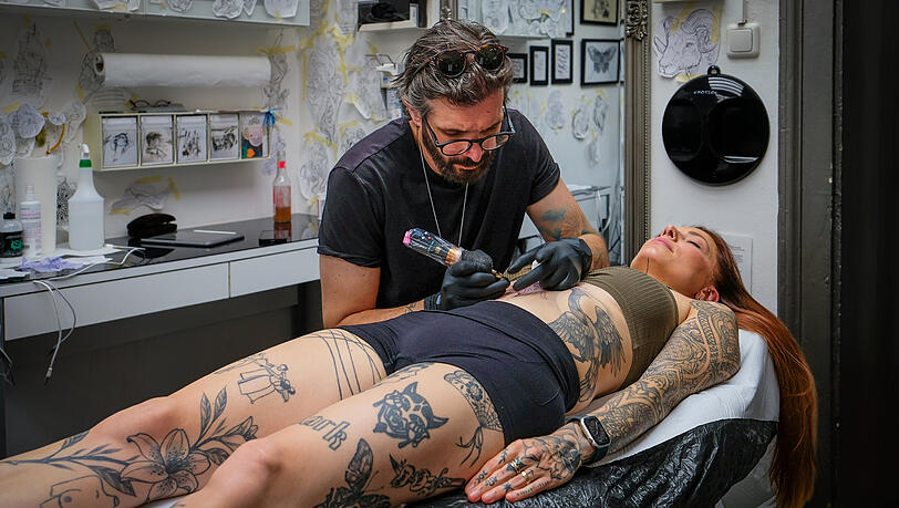 Larissa Oswald schlie&szlig;t die Augen, w&auml;hrend Kosta Vergidis (49) konzentriert die Nadel auf ihren Bauch setzt. Er darf der 38-J&auml;hrigen an diesem Tag ein neues Tattoo stechen &ndash; eine filigrane Blume. Seit Jahren kommt Oswald hierher, um sich neue Motive unter die Haut stechen zu lassen.