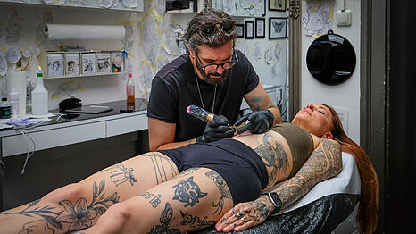 Larissa Oswald schlie&szlig;t die Augen, w&auml;hrend Kosta Vergidis (49) konzentriert die Nadel auf ihren Bauch setzt. Er darf der 38-J&auml;hrigen an diesem Tag ein neues Tattoo stechen &ndash; eine filigrane Blume. Seit Jahren kommt Oswald hierher, um sich neue Motive unter die Haut stechen zu lassen.