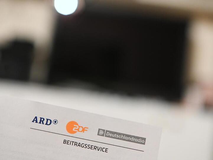 Ein Anschreiben des Beitragsservice für die Rundfunkgebühren ist vor einem Fernseher zu sehen. Foto: Nicolas Armer/dpa/Archivbild