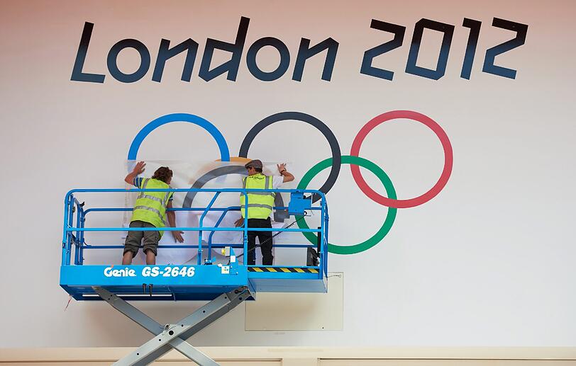Arbeiter bringen die Olympischen Ringe an einem Gebäude an.