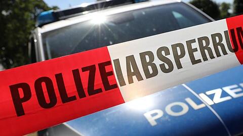 Eine Polizeiabsperrung hängt vor einem Polizeiauto.