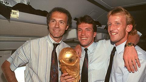 Im Flugzeug präsentieren der damalige DFB-Teamchef Franz Beckenbauer (l), Lothar Matthäus (M) und Andreas Brehme den WM-Pokal.
