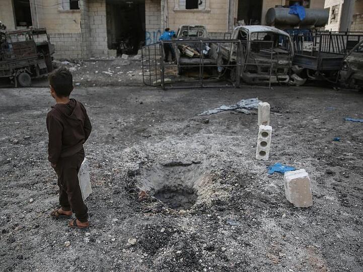 Ein Kind geht in Idlib nach einem Raketenbeschuss an einer Einschlagstelle im Boden vorbei.