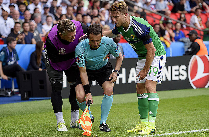 Bastian Schweinsteiger und Nordirlands Jamie Ward (rechts) helfen dem französischen Schiedsrichter-Assistenten Fréderic Cano (Mitte) auf die Beine.