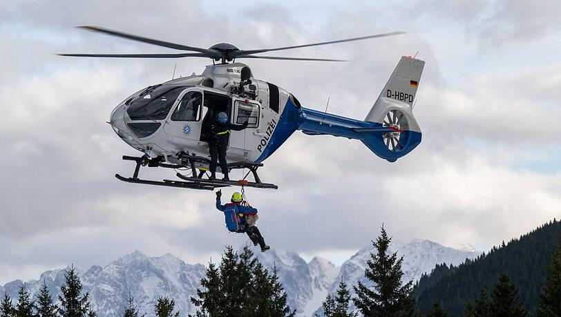 Ein Hundeführer der Bergrettung hängt mit Hilfe eines Seils an einem Hubschrauber.