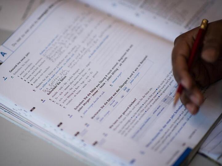 Eine Frau schreibt in ein Lehrbuch eines Integrationskurses. Foto: Sophia Kembowski/Archiv