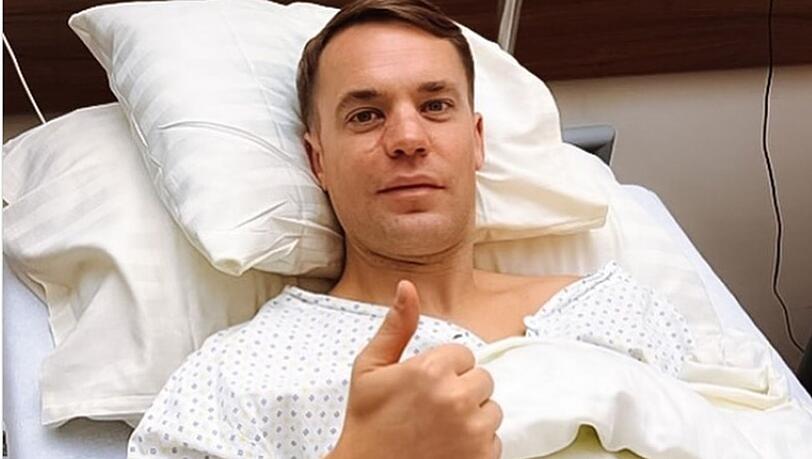 Manuel Neuer, Torwart beim FC Bayern, hält im Krankenhausbett nach seiner Operation am Knie den Daumen nach oben.