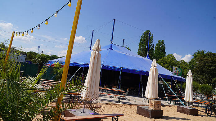 Die Aussichten sind sonnig: In der Half Moon Bar auf dem Tollwood macht man es sich auf Bierbänken oder mit einem Getränk in der Hand auf Liegestühlen im Sand gemütlich. Abends findet im Zelt die Silent Disco statt. Dort tanzen die Besucher zur Musik aus Kopfhörern. Das lädt auch zum Zuschauen ein.