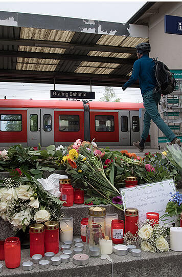 Blumen und Kerzen liegen am Bahnhof in Grafing um ein handgemaltes Schild. Bei einer Messerattacke waren am Dienstag drei Personen verletzt und ein Mann getötet worden.