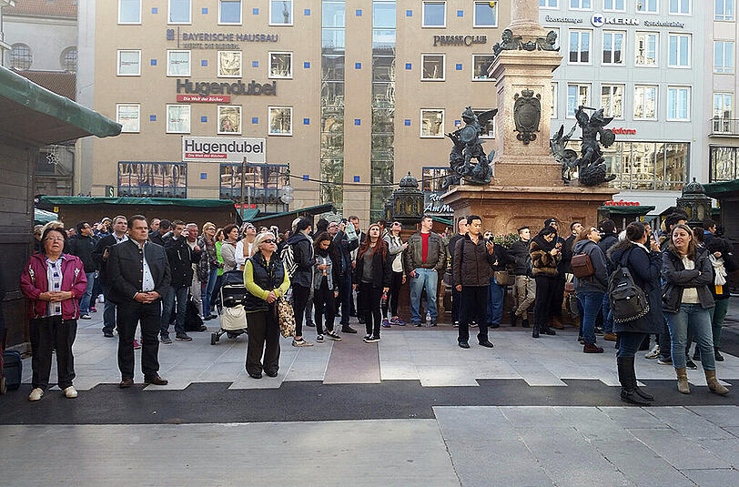 Am Marienplatz halten Münchenr ein und gedenken, während um sie herum der Tourismus weitergeht.