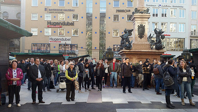 Am Marienplatz halten Münchenr ein und gedenken, während um sie herum der Tourismus weitergeht.