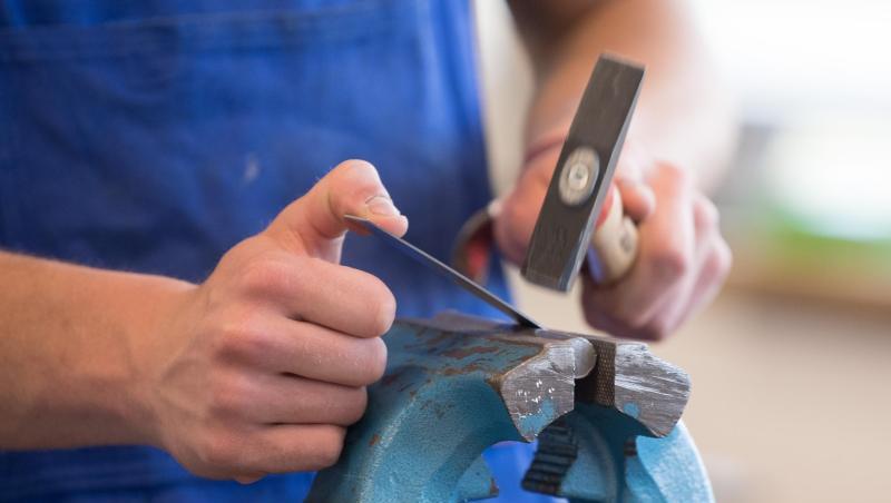 Ein Auszubildender steht mit einem Hammer an einem Schraubstock. Betriebe, die Azubis von insolvent gegangenen Firmen übernehmen, sollen eine staatliche Prämie bekommen. Ein Auszubildender steht mit einem Hammer an einem Schraubstock. Betriebe, die Azubis von insolvent gegangenen Firmen übernehmen, sollen eine staatliche Prämie bekommen.