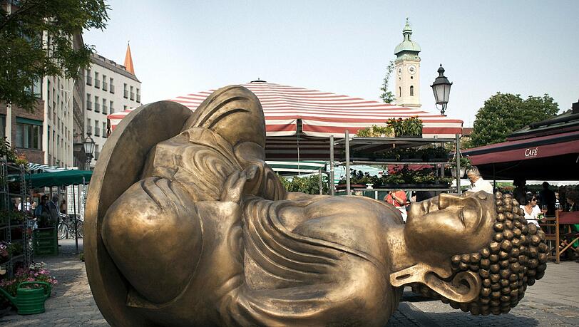 Den Münchner Viktualienmarkt ziert seit dem 8. Mai ein schräger Buddha-Skulptur "Made in Dresden", das Projekt des Malaysischen Künstlers Han Chong. Der unecht anmutende goldene Farbton der Skulptur und ihr einfaches Design erinnern an typische Souvenirartikel – ein kritischer Verweis auf die industrielle Massenproduktion als Phänomen unserer Zeit sowie auf die weitgehend unbekannte Tatsache, dass Billigartikel für den asiatischen Raum in Europa hergestellt werden. Den Münchner Viktualienmarkt ziert seit dem 8. Mai ein schräger Buddha-Skulptur "Made in Dresden", das Projekt des Malaysischen Künstlers Han Chong. Der unecht anmutende goldene Farbton der Skulptur und ihr einfaches Design erinnern an typische Souvenirartikel – ein kritischer Verweis auf die industrielle Massenproduktion als Phänomen unserer Zeit sowie auf die weitgehend unbekannte Tatsache, dass Billigartikel für den asiatischen Raum in Europa hergestellt werden.