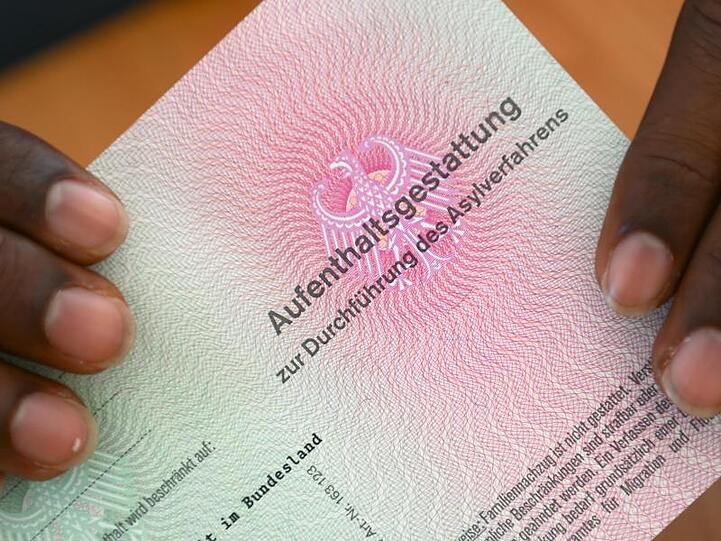 Ein somalischer Flüchtling hält eine Aufenthaltsgestattung in den Händen. Foto: Arne Dedert/Archiv