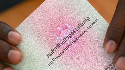 Ein somalischer Flüchtling hält eine Aufenthaltsgestattung in den Händen. Foto: Arne Dedert/Archiv
