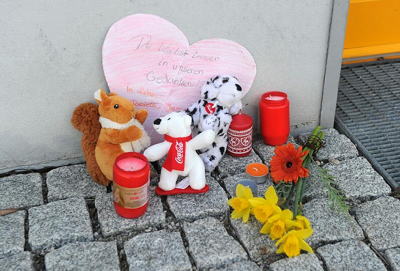 Blumen, Kerzen, Stofftiere und ein Papierherz mit der Aufschrift "Du bleibst immer in unseren Gedanken" liegen in Unterföhring vor einem Hauseingang an Gedenken an die 16-jährige Larissa.