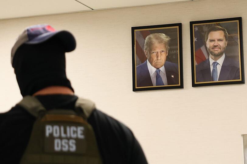 Ein New Yorker Bundesagent geht an Portärts von US-Präsident Trum und Vizepräsident JD Vance vorbei. Die US-Regierung geht konsequent gegen Einwanderer ohne Aufenthaltstitel vor. Ein New Yorker Bundesagent geht an Portärts von US-Präsident Trum und Vizepräsident JD Vance vorbei. Die US-Regierung geht konsequent gegen Einwanderer ohne Aufenthaltstitel vor.