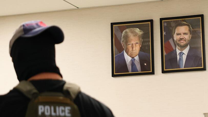 Ein New Yorker Bundesagent geht an Portärts von US-Präsident Trum und Vizepräsident JD Vance vorbei. Die US-Regierung geht konsequent gegen Einwanderer ohne Aufenthaltstitel vor. Ein New Yorker Bundesagent geht an Portärts von US-Präsident Trum und Vizepräsident JD Vance vorbei. Die US-Regierung geht konsequent gegen Einwanderer ohne Aufenthaltstitel vor.