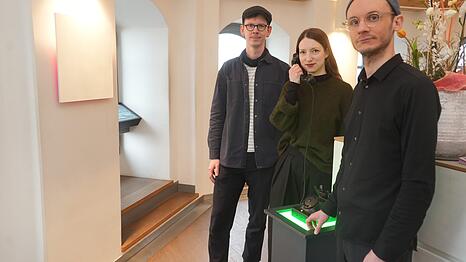 Die Klang-Installation im S&uuml;dturm der Frauenkirche, mit den K&uuml;nstlern (v.l.) Luis Wei&szlig;, Nathalie Brum und Lukas Sch&auml;fer. Brum h&auml;lt den H&ouml;rer des Memophons in der Hand. Darin sind 200 Audio-Aufzeichnungen zu h&ouml;ren. Links an der Wand: schwingende Kiefernholzplatte.