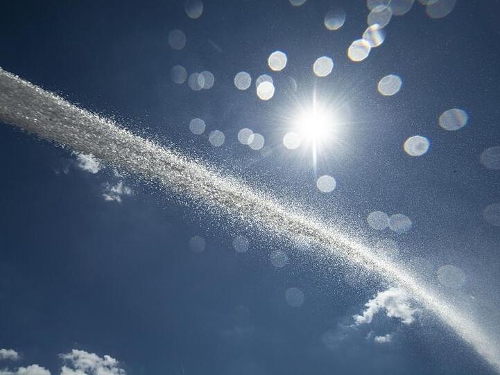 Der Wasserstrahl eines Bewässerungsfahrzeuges zeichnet sich gegen den blauen Himmel ab. Foto: Boris Roessler/Archivbild