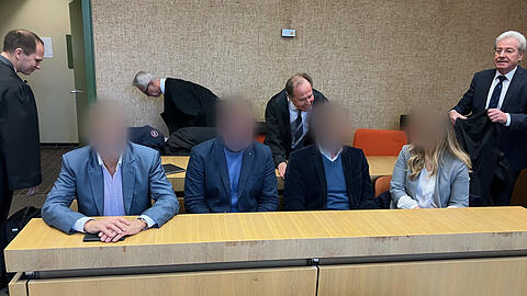 Prozess um Impf-Aktion: Die vier Angeklagten sitzen im Amtsgericht München nebeneinander auf der Anklagebank, im Hintergrund deren Anwälte (v.l.n.r.) Michael Pösl, Hartmut Girshausen, Thomas Pfister und Reinhard Debernitz.