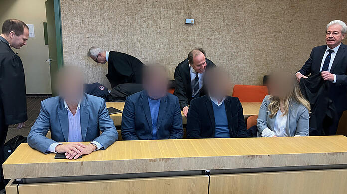 Prozess um Impf-Aktion: Die vier Angeklagten sitzen im Amtsgericht München nebeneinander auf der Anklagebank, im Hintergrund deren Anwälte (v.l.n.r.) Michael Pösl, Hartmut Girshausen, Thomas Pfister und Reinhard Debernitz.