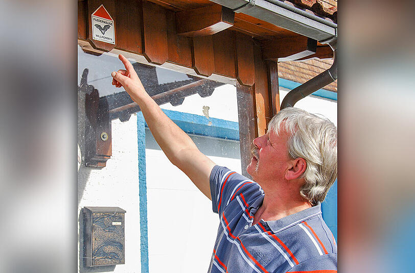 Alexander Rist zeigt auf die Plakette &bdquo;Fledermäuse willkommen&ldquo;.