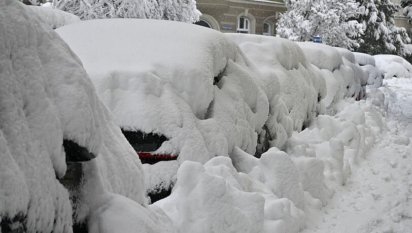 Eine dicke Schneeschicht liegt auf parkenden Autos in München.