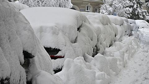 Eine dicke Schneeschicht liegt auf parkenden Autos in München.