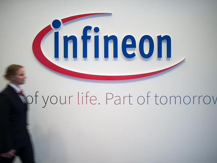 Eine Frau geht an einem Logo von Infineon vorbei. Foto: Matthias Balk/dpa