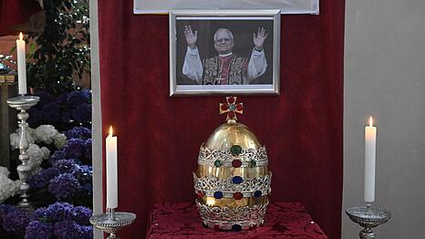 In der Münchner Stadtpfarrkirche ist die Tiara der Petrusfigur vor einem Bild des neuen Papstes Leo XIV. zu sehen.